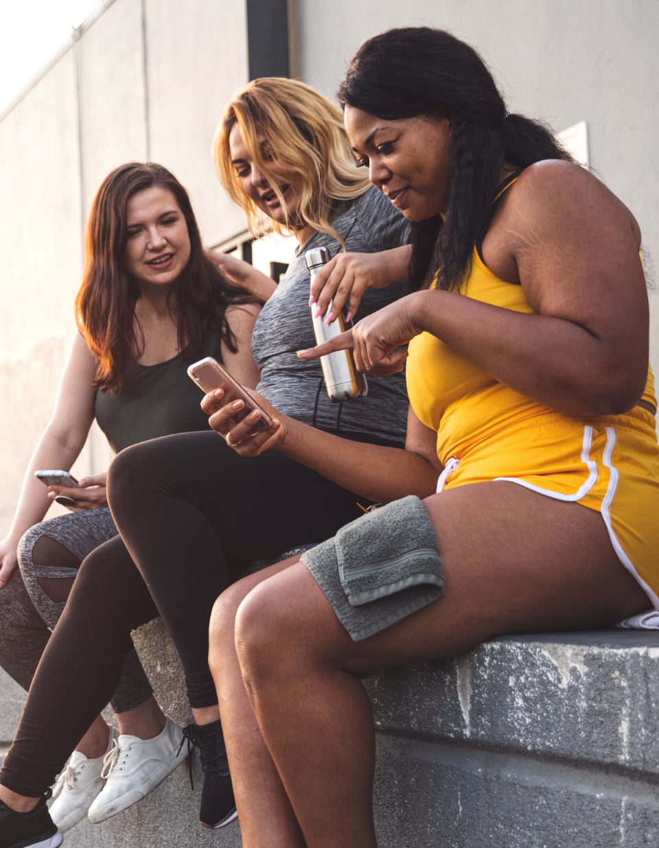 A group of 3 women socialising with eachother outside looking at one of their phones